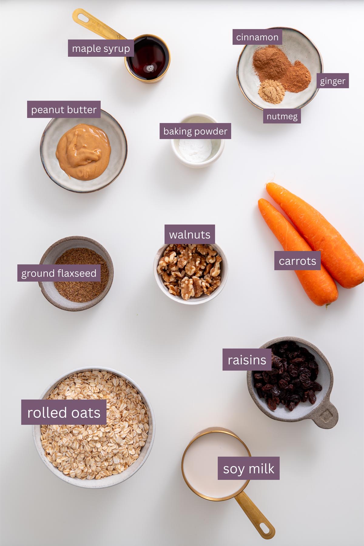Labeled ingredients for carrot cake baked oats including oats, carrots, walnuts, raisins, soy milk, peanut butter, flaxseed, baking powder, maple syrup, and spices