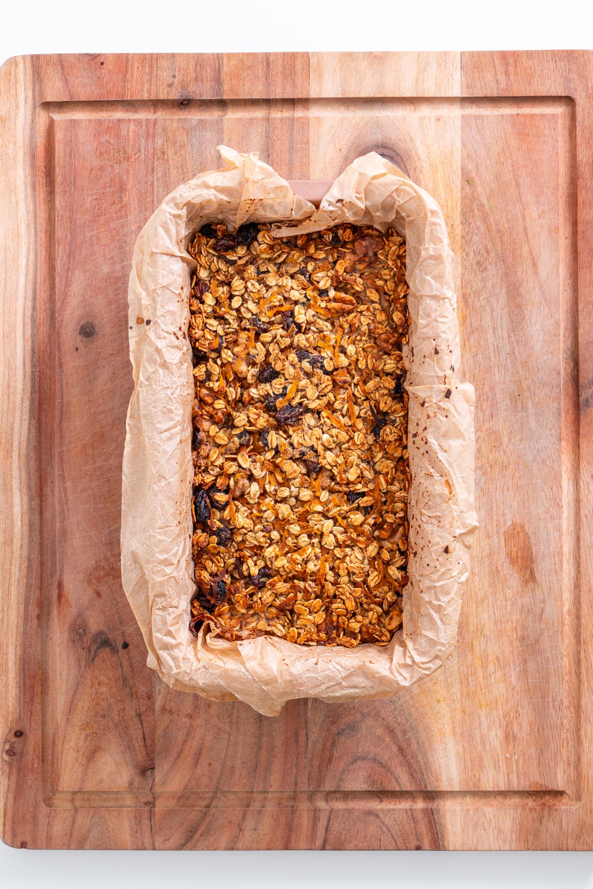 Golden baked carrot cake baked oats in a parchment-lined loaf pan on a wooden board