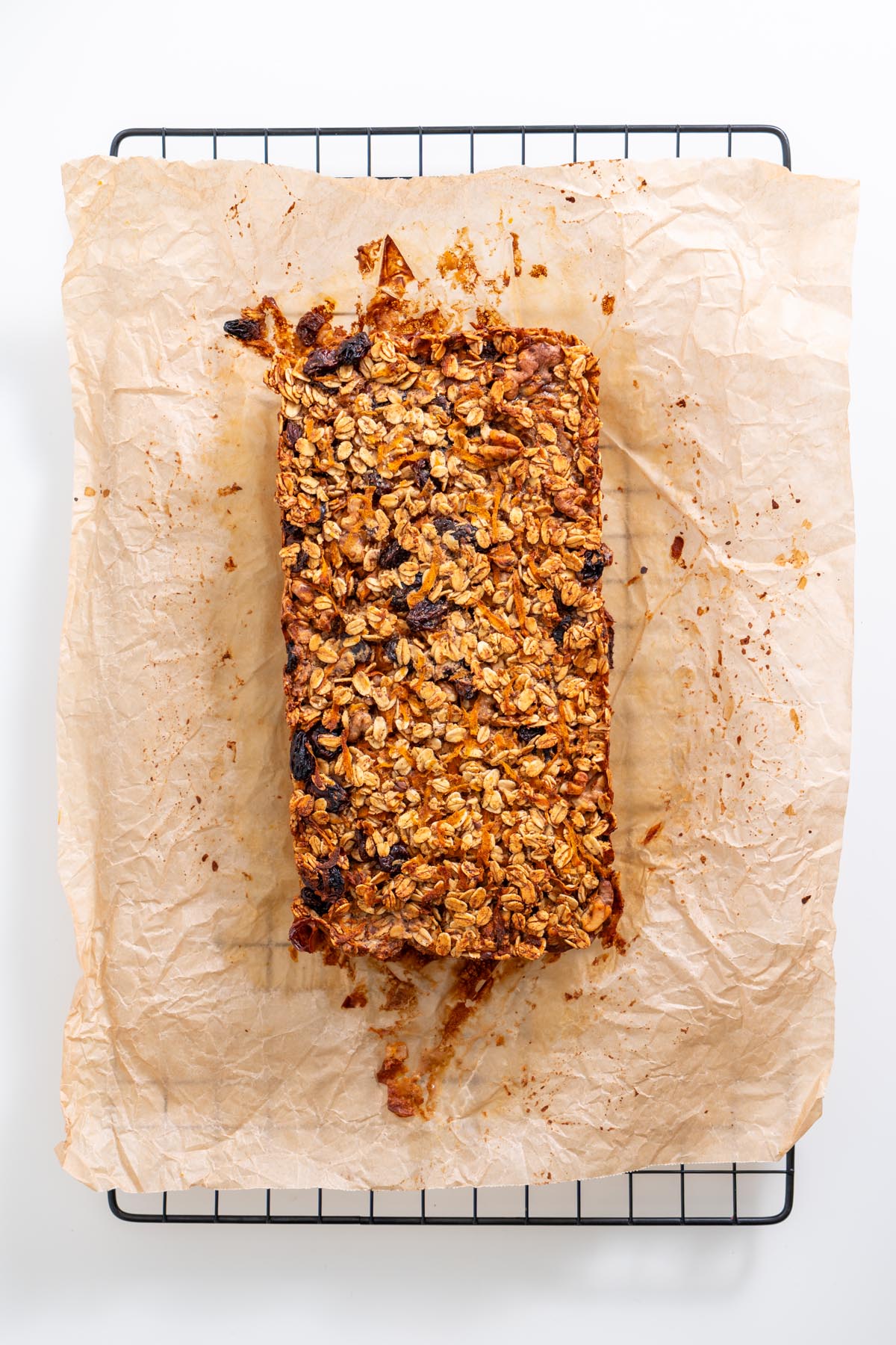 Loaf of baked carrot cake oats on parchment paper resting on a cooling rack