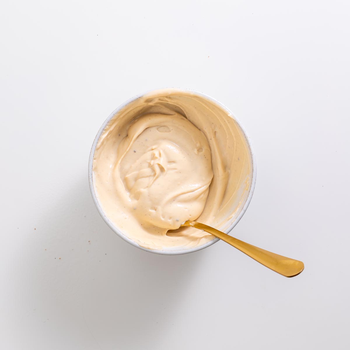 Small bowl of creamy protein yogurt icing with a gold spoon on a white background