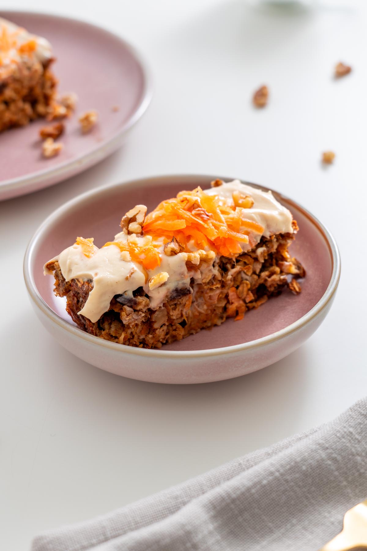 Slice of carrot cake baked oats with protein icing and shredded carrot topping on a pink plate