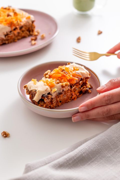 Sarah Cobacho holding a plate with a slice of carrot cake baked oats topped with protein yogurt icing and shredded carrots