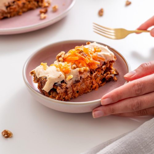 Sarah Cobacho holding a plate with a slice of carrot cake baked oats topped with protein yogurt icing and shredded carrots