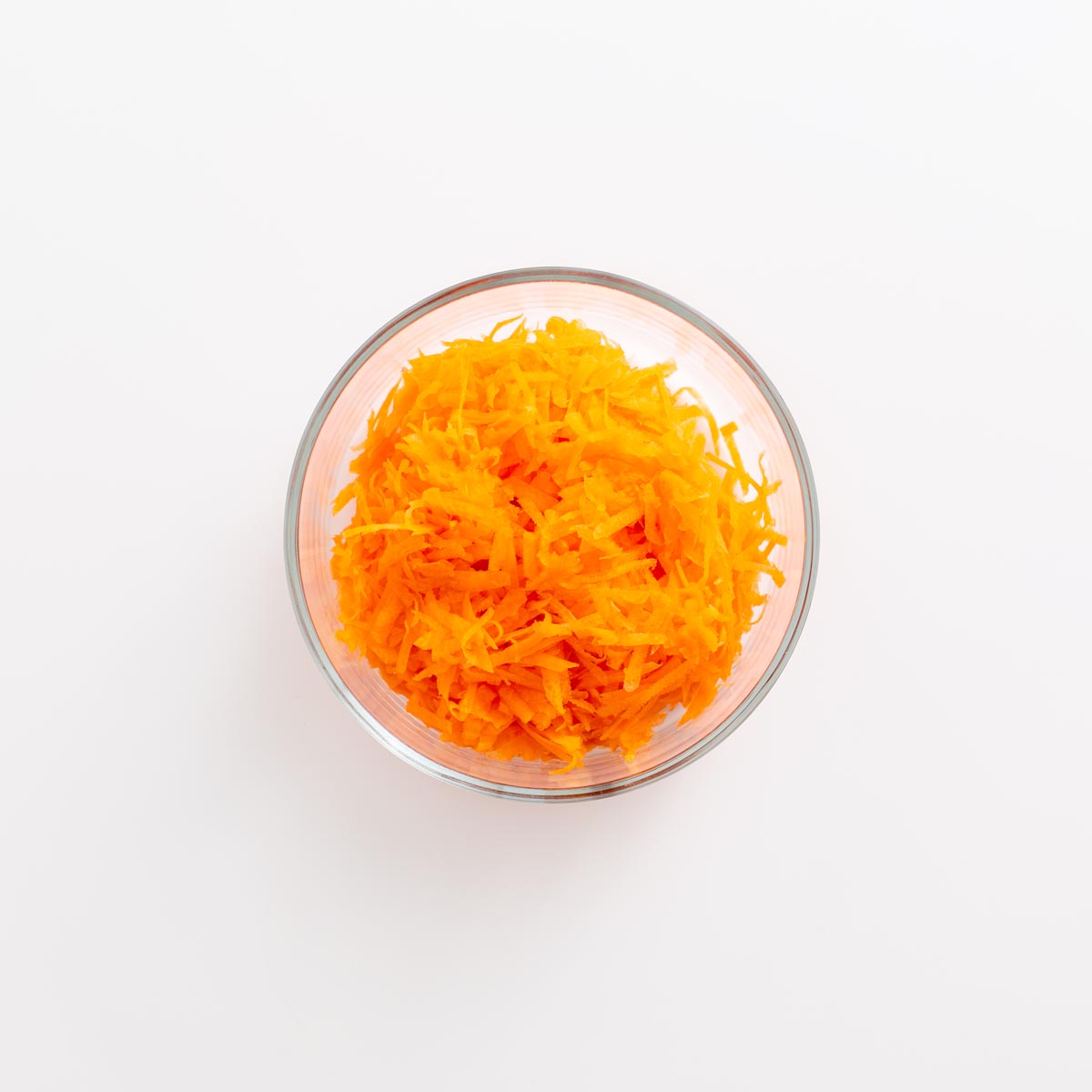 Bowl of freshly grated carrots on a white background