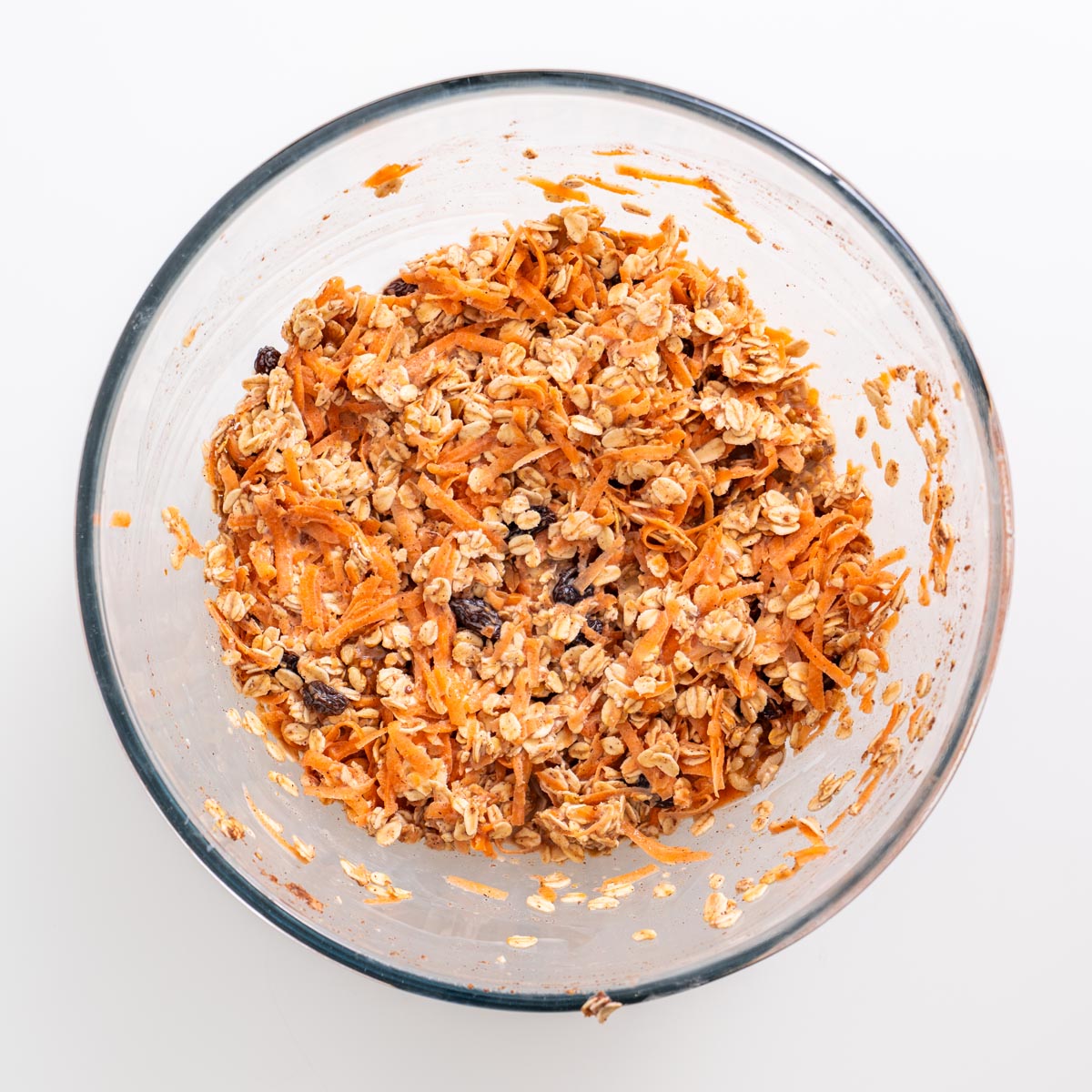 Mixing bowl filled with oats, shredded carrots, raisins, and walnuts combined together