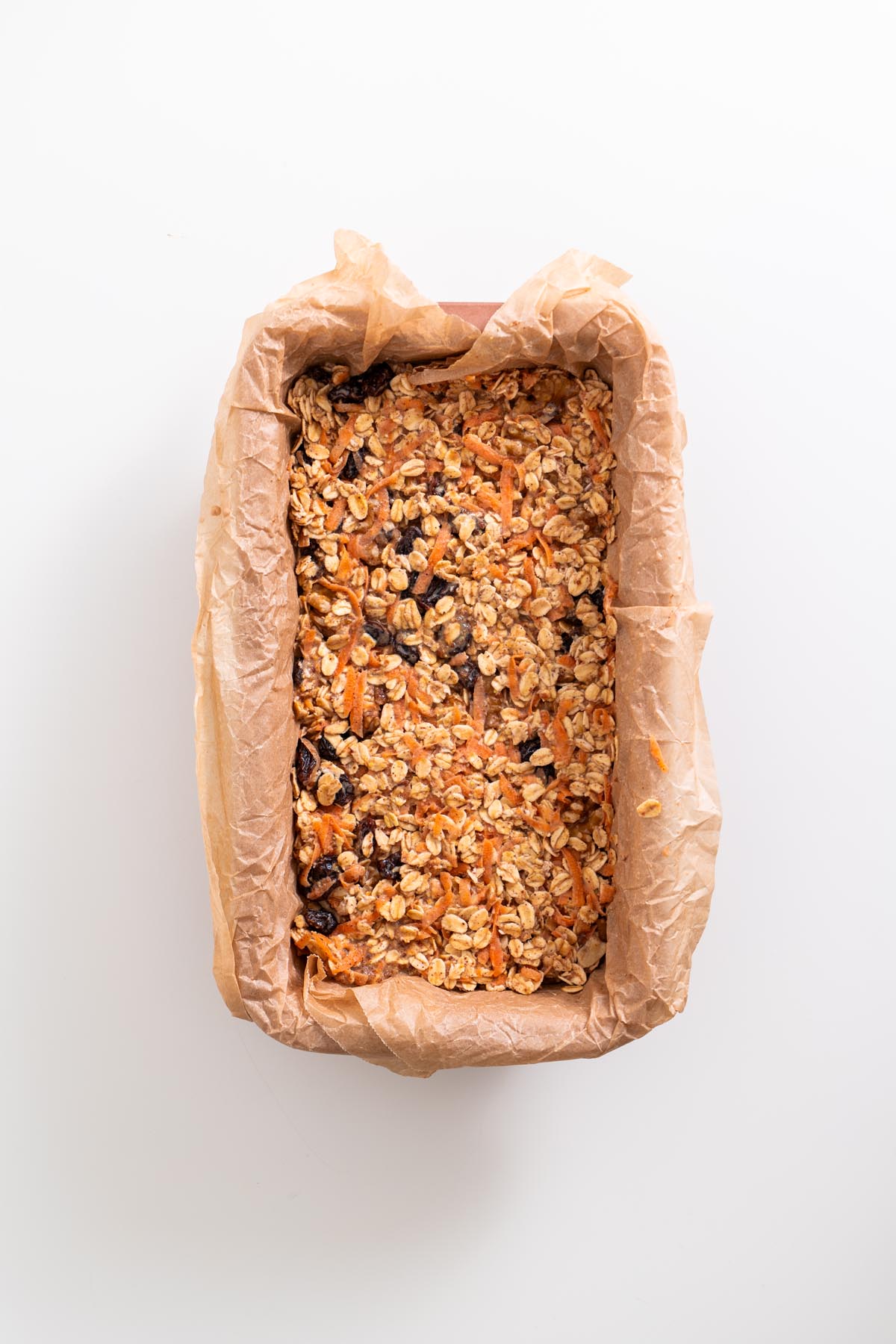 Unbaked carrot cake baked oats mixture spread evenly in a parchment-lined loaf pan