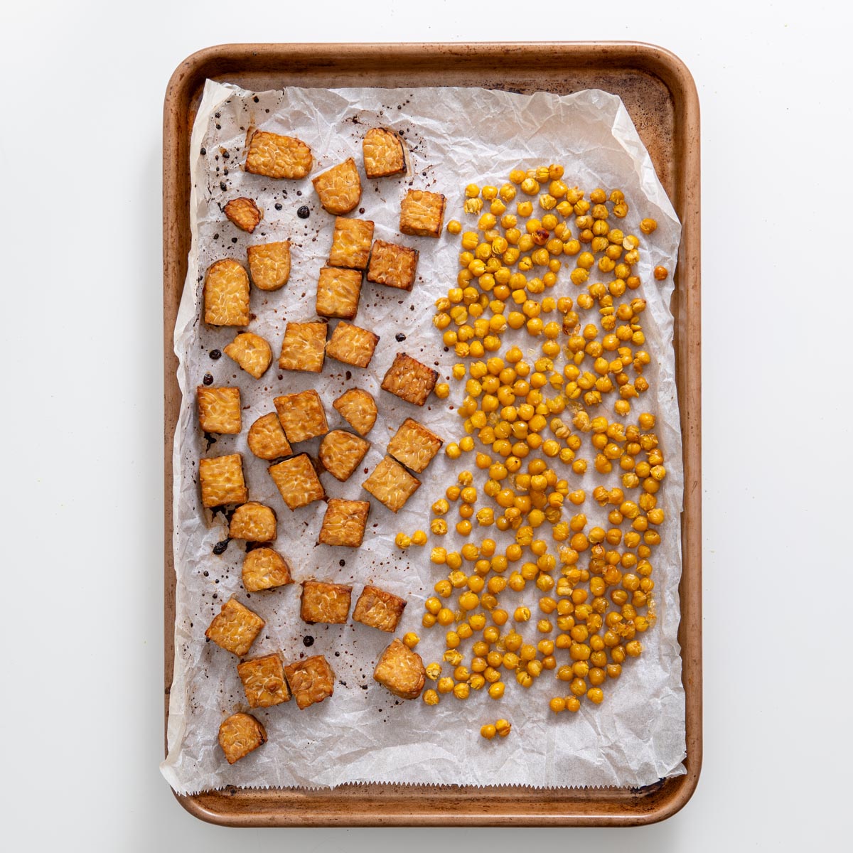 Baking tray with roasted tempeh cubes and crispy chickpeas on parchment paper.