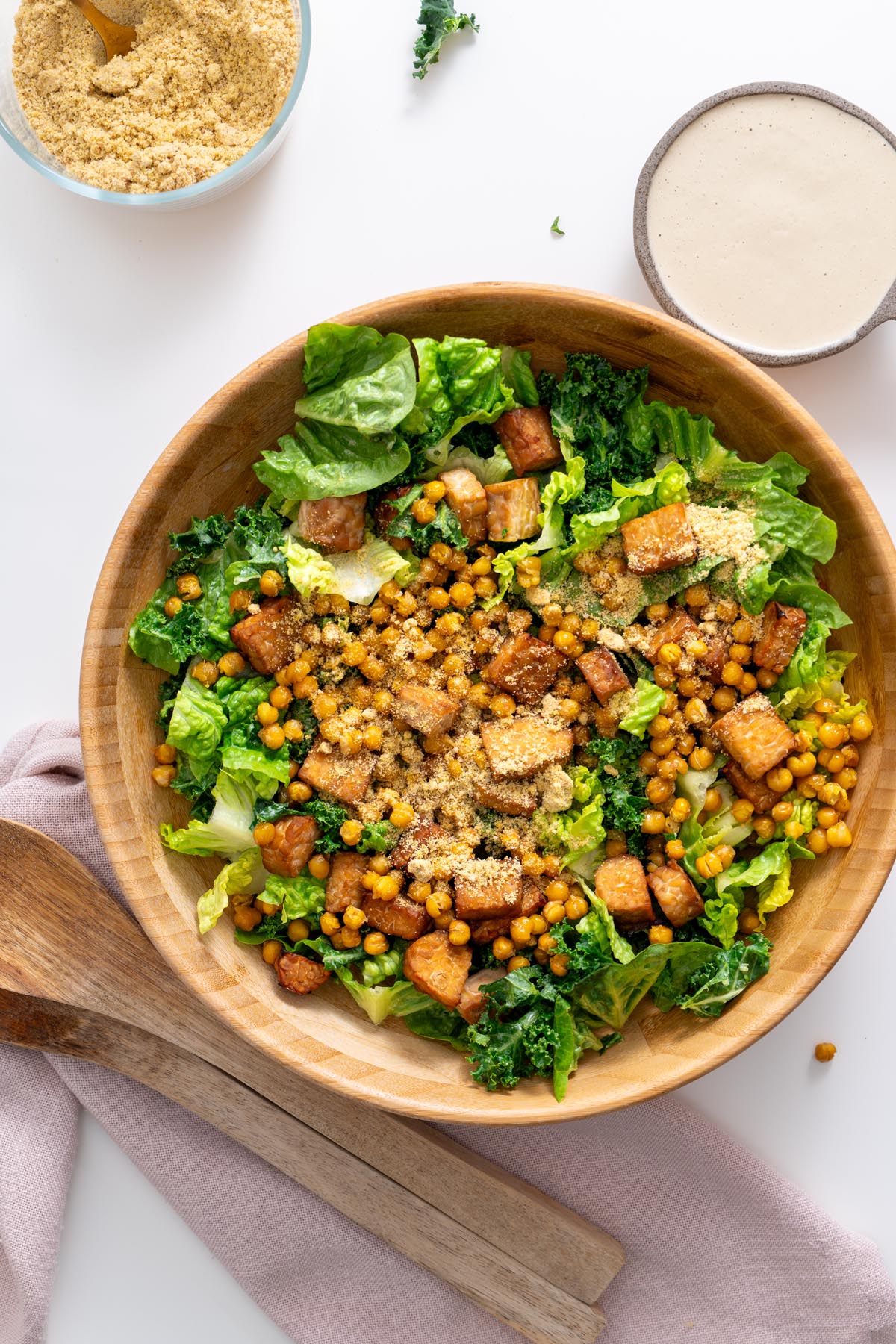 Large wooden bowl filled with vegan Caesar salad topped with crispy tempeh, roasted chickpeas, and dairy-free parmesan.
