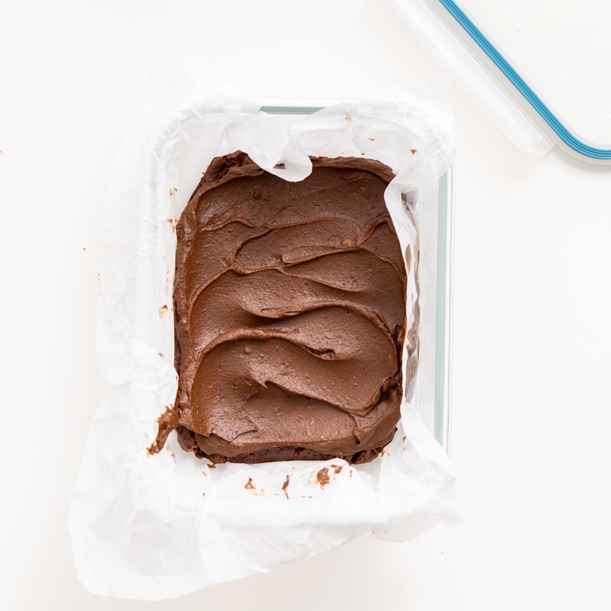 Tray of fudgy no-bake brownies lined with parchment, topped with avocado ganache