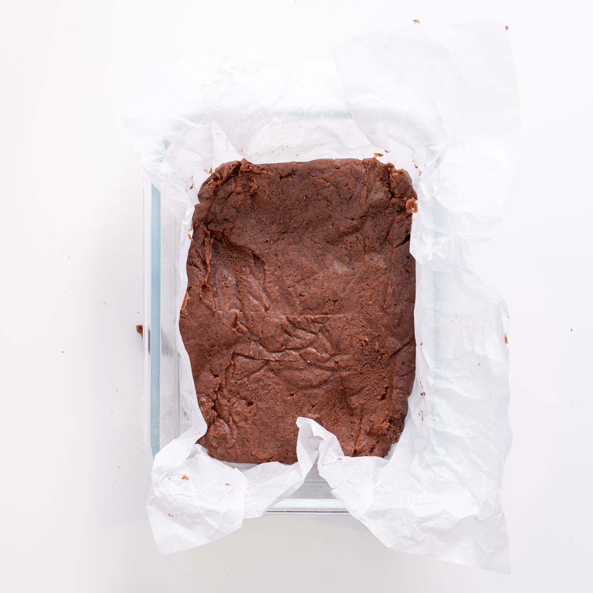 Brownie base pressed into a parchment-lined tray before adding ganache