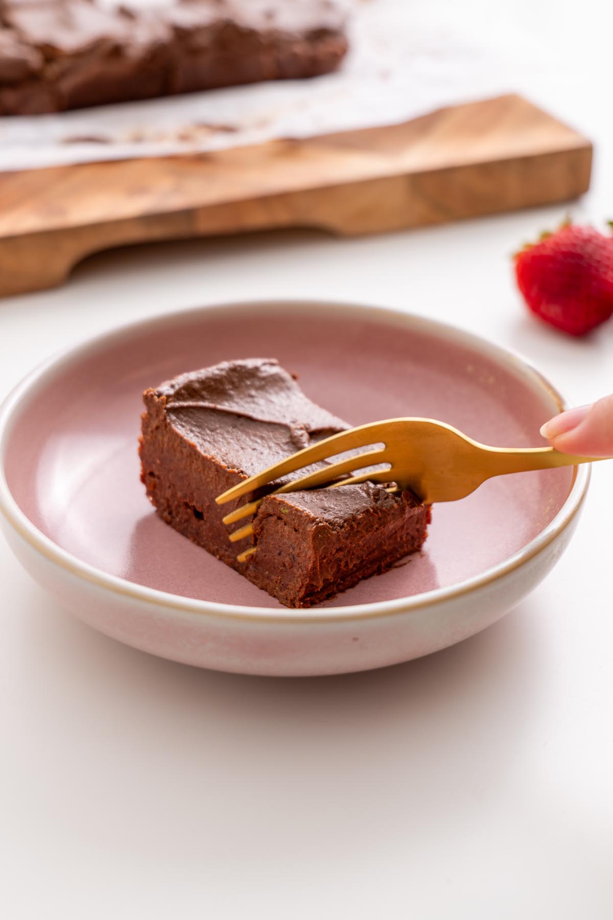 Sarah Cobacho holding a golden fork over a fudgy no-bake brownie slice on a pink plate