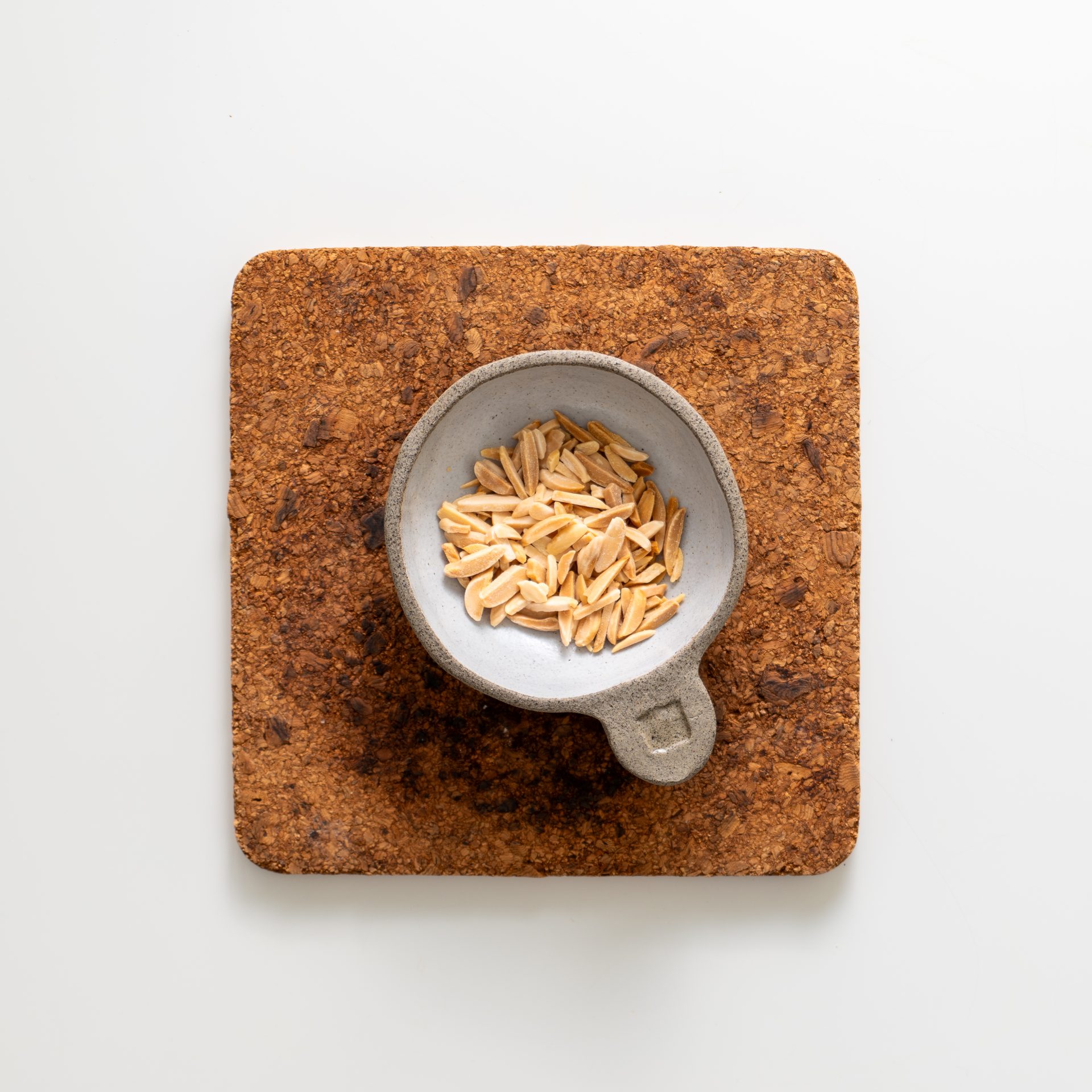 Lightly toasted slivered almonds in a small dish on a cork board