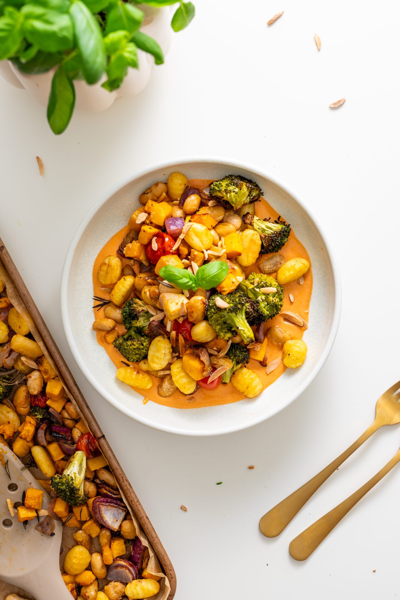Bowl of roasted gnocchi, pumpkin, broccoli, onion, and tomatoes served over creamy tahini sauce, garnished with basil