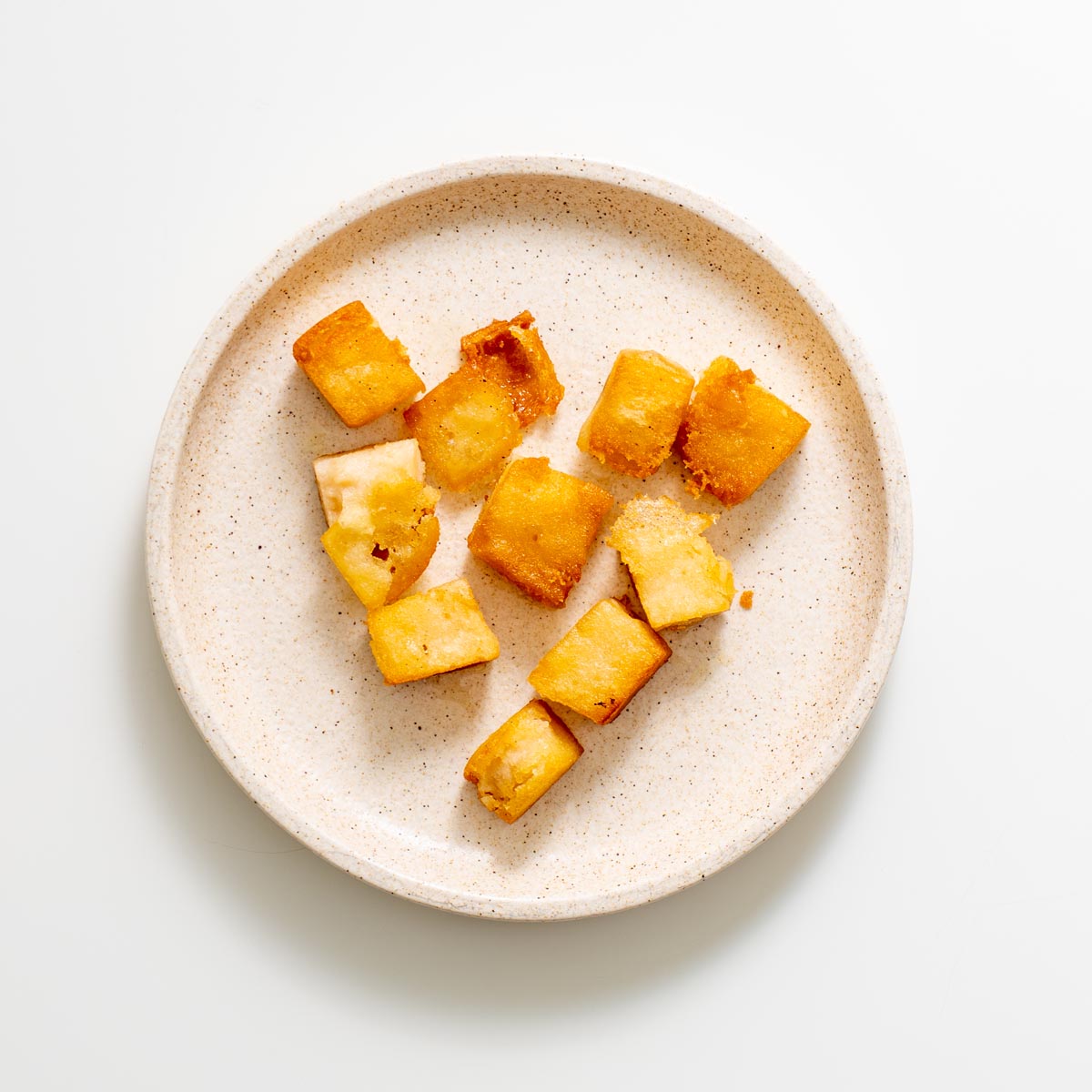 Golden brown crispy red lentil tofu cubes served on a speckled ceramic plate