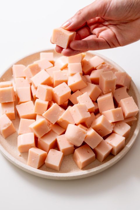 Sarah Cobacho holding a cube of firm red lentil tofu over a plate of tofu pieces