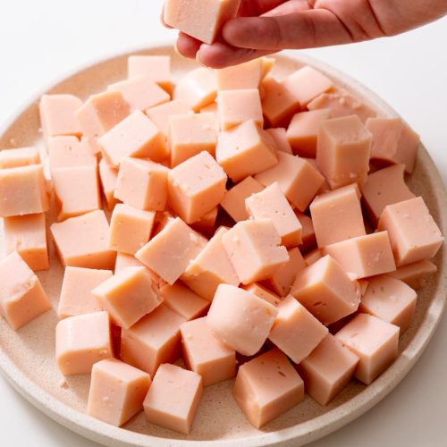 Sarah Cobacho holding a cube of firm red lentil tofu over a plate of tofu pieces