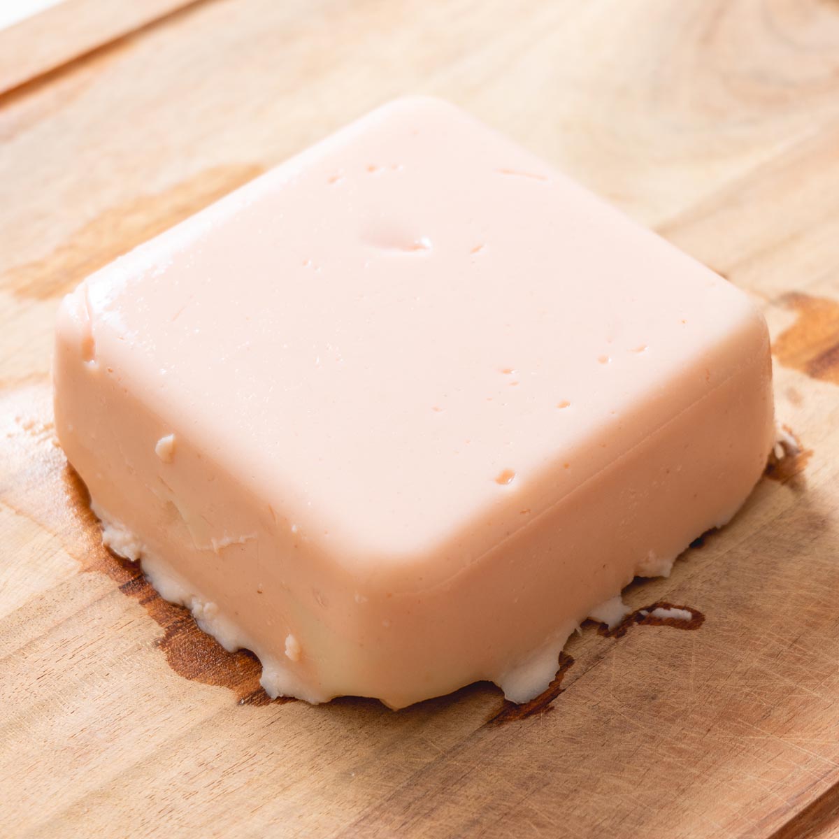 Block of red lentil tofu resting on wooden board with smooth firm texture