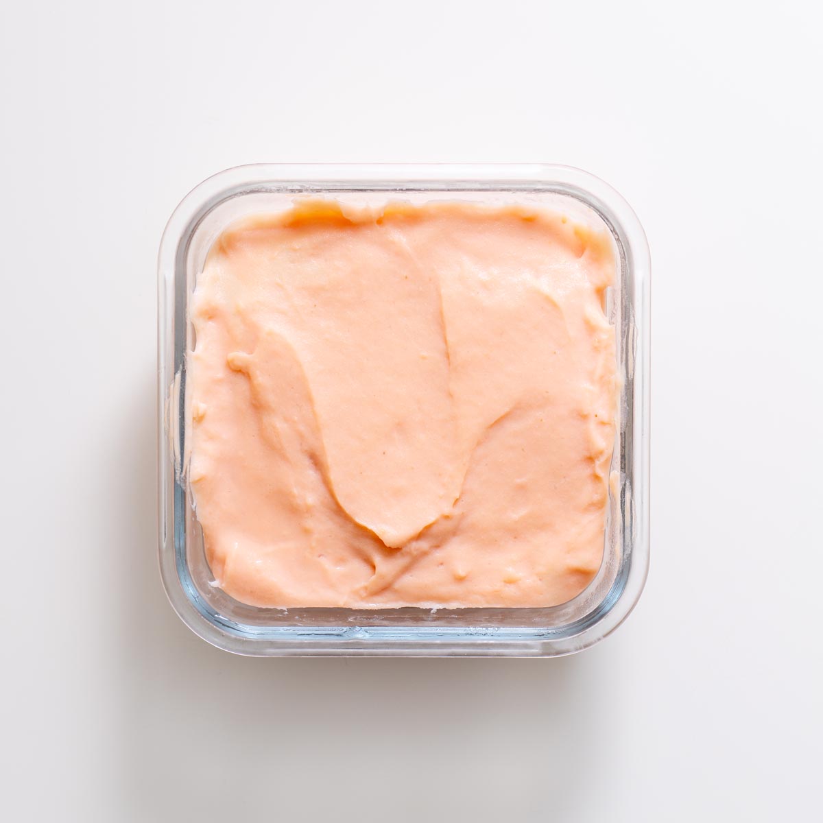 Glass container filled with freshly set red lentil tofu on a white background