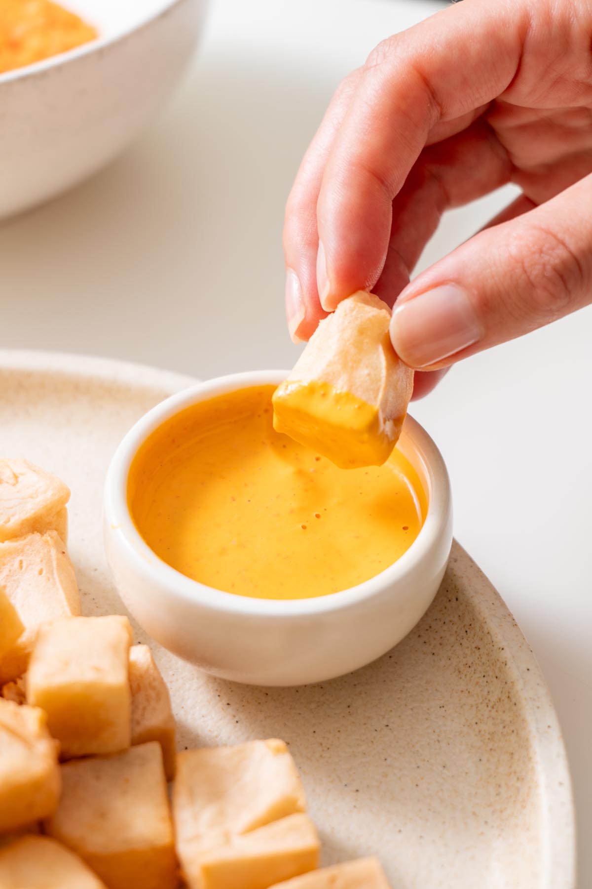 Close-up of Sarah Cobacho dipping red lentil tofu cube into bright orange sauce