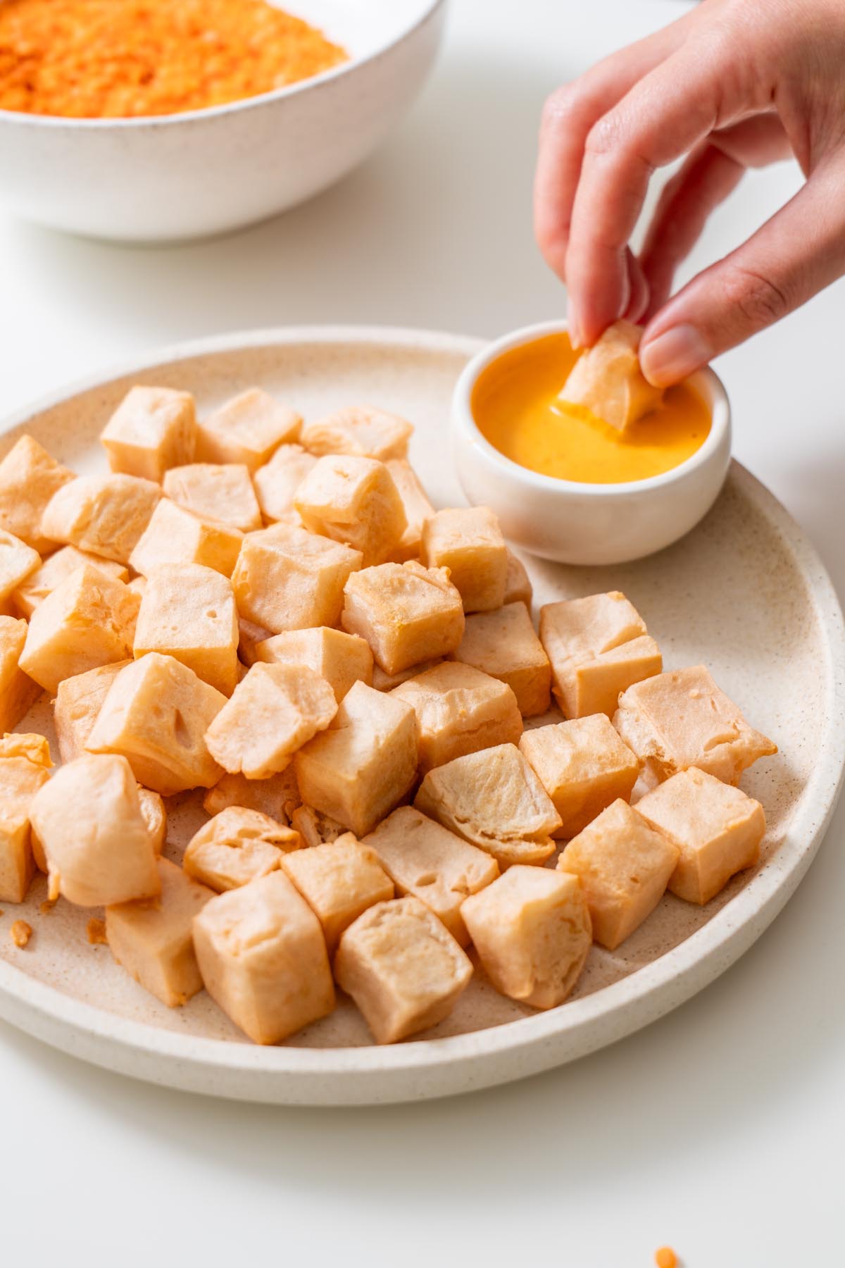 Sarah Cobacho dipping a cube of red lentil tofu into golden sauce
