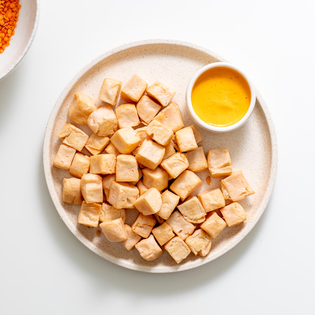 Plate of cubed red lentil tofu served with a small bowl of dipping sauce
