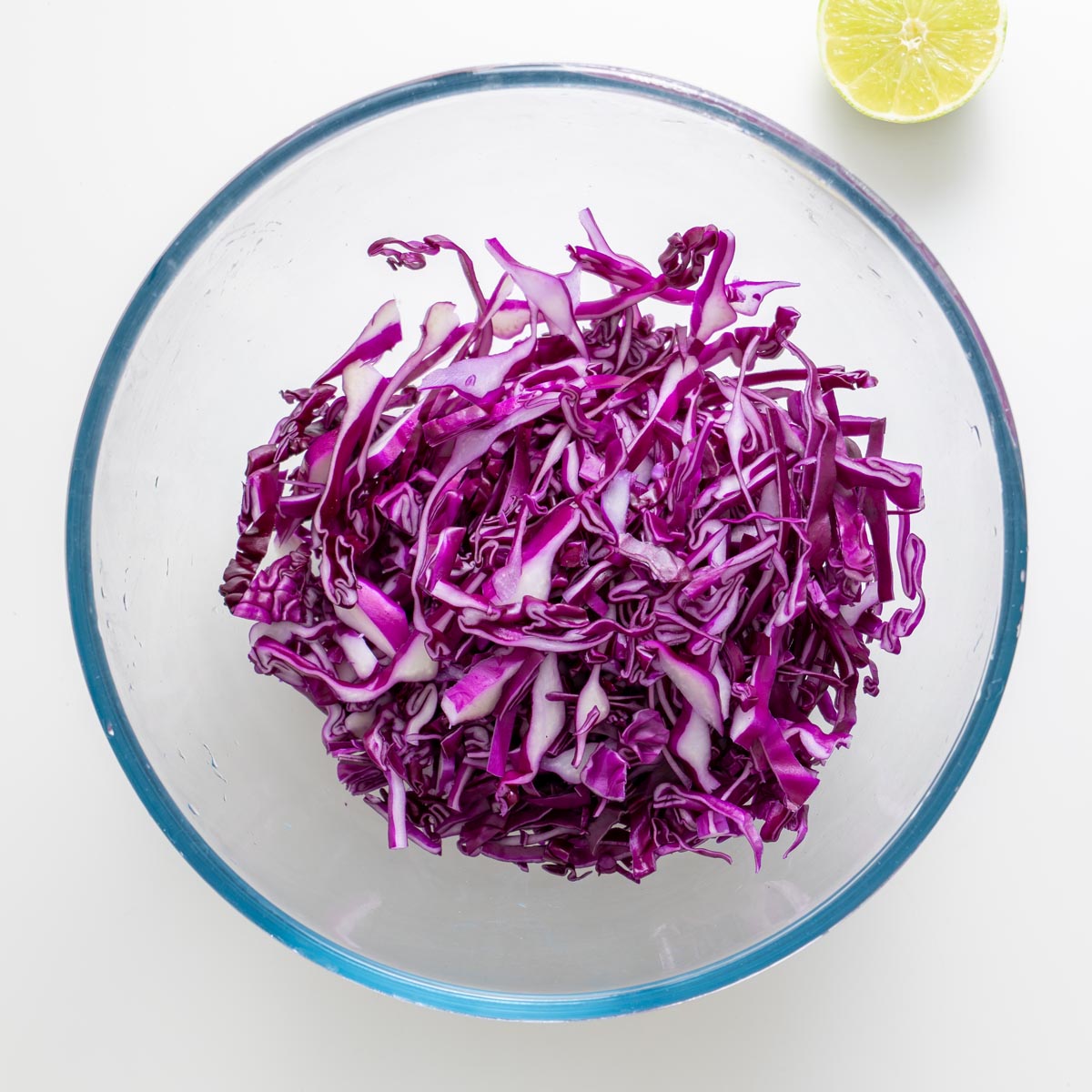 Shredded purple cabbage in a glass bowl with a halved lime on the side