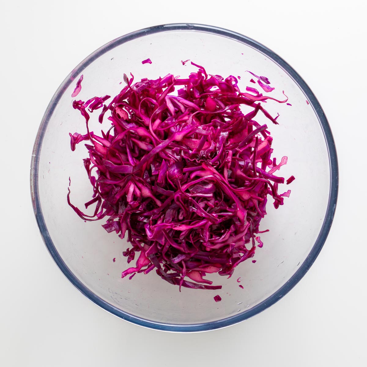 Shredded purple cabbage for peanut vermicelli salad jars in a clear glass bowl on a white surface