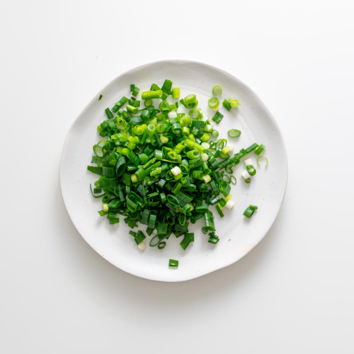 Finely sliced scallions on a white plate for peanut vermicelli salad jars