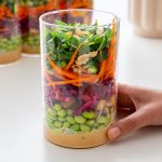 Hand holding a glass jar filled with layered peanut vermicelli salad, with more jars in the background
