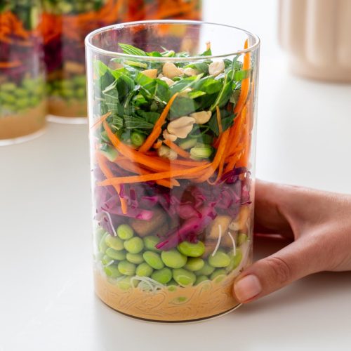 Hand holding a glass jar filled with layered peanut vermicelli salad, with more jars in the background