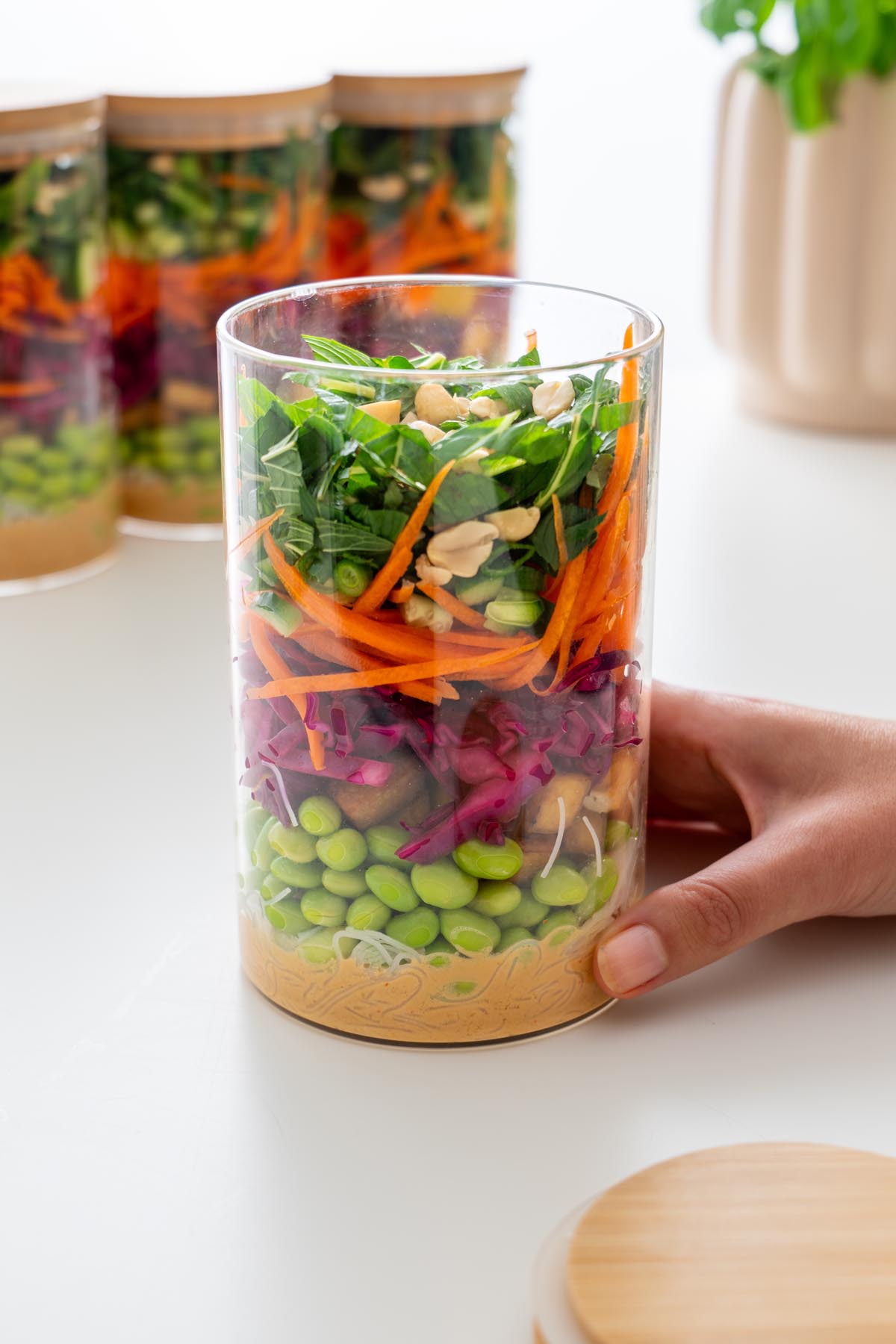 Hand holding a glass jar filled with layered peanut vermicelli salad, with more jars in the background