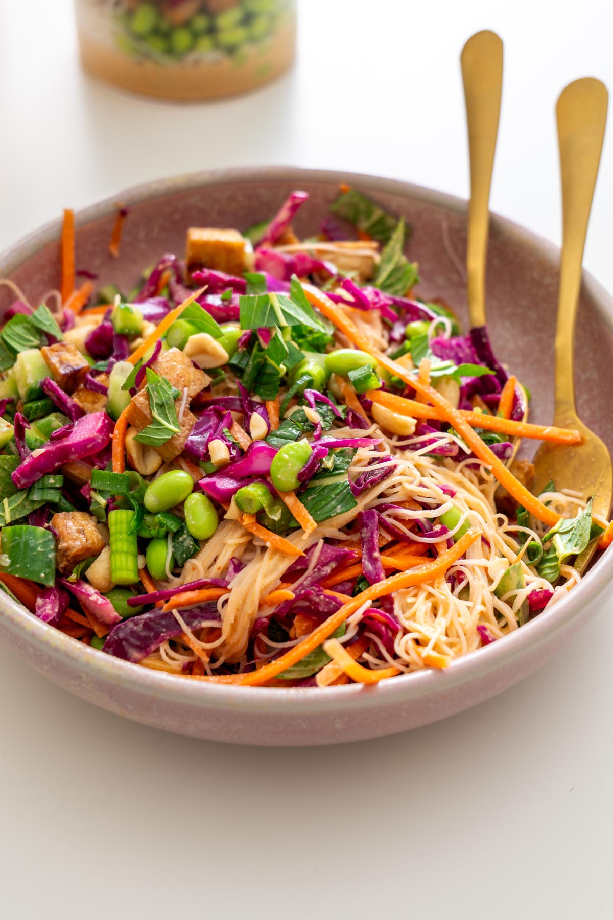 Bowl of peanut vermicelli salad mixed with tofu, edamame, cabbage, carrots, cucumbers, mint, and peanuts, with two gold forks