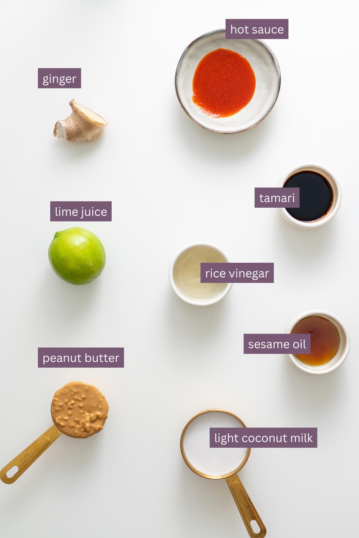 Peanut dressing ingredients including ginger, lime juice, peanut butter, hot sauce, tamari, rice vinegar, sesame oil, and light coconut milk on a white surface