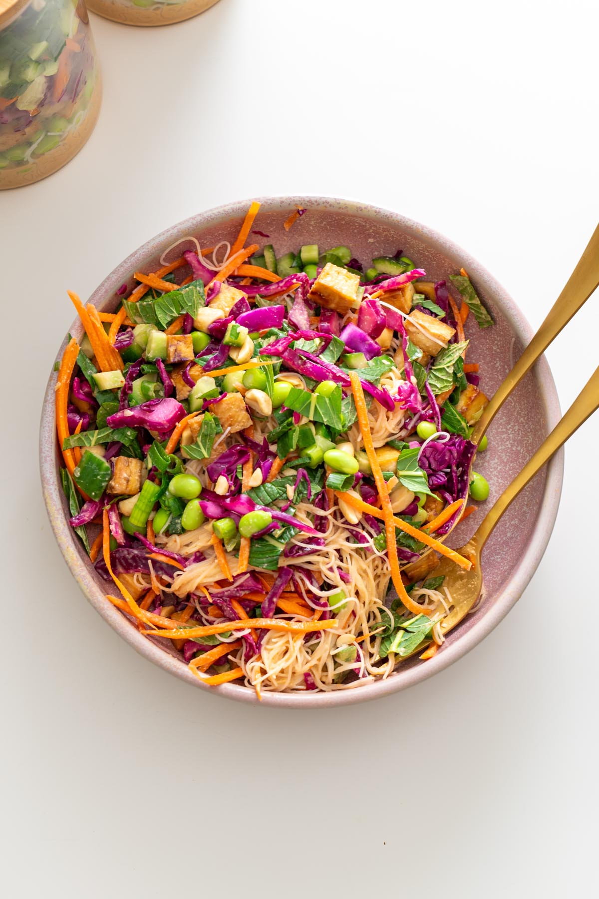 Overhead view of peanut vermicelli salad in a pink bowl with tofu, cabbage, carrots, cucumbers, edamame, and mint