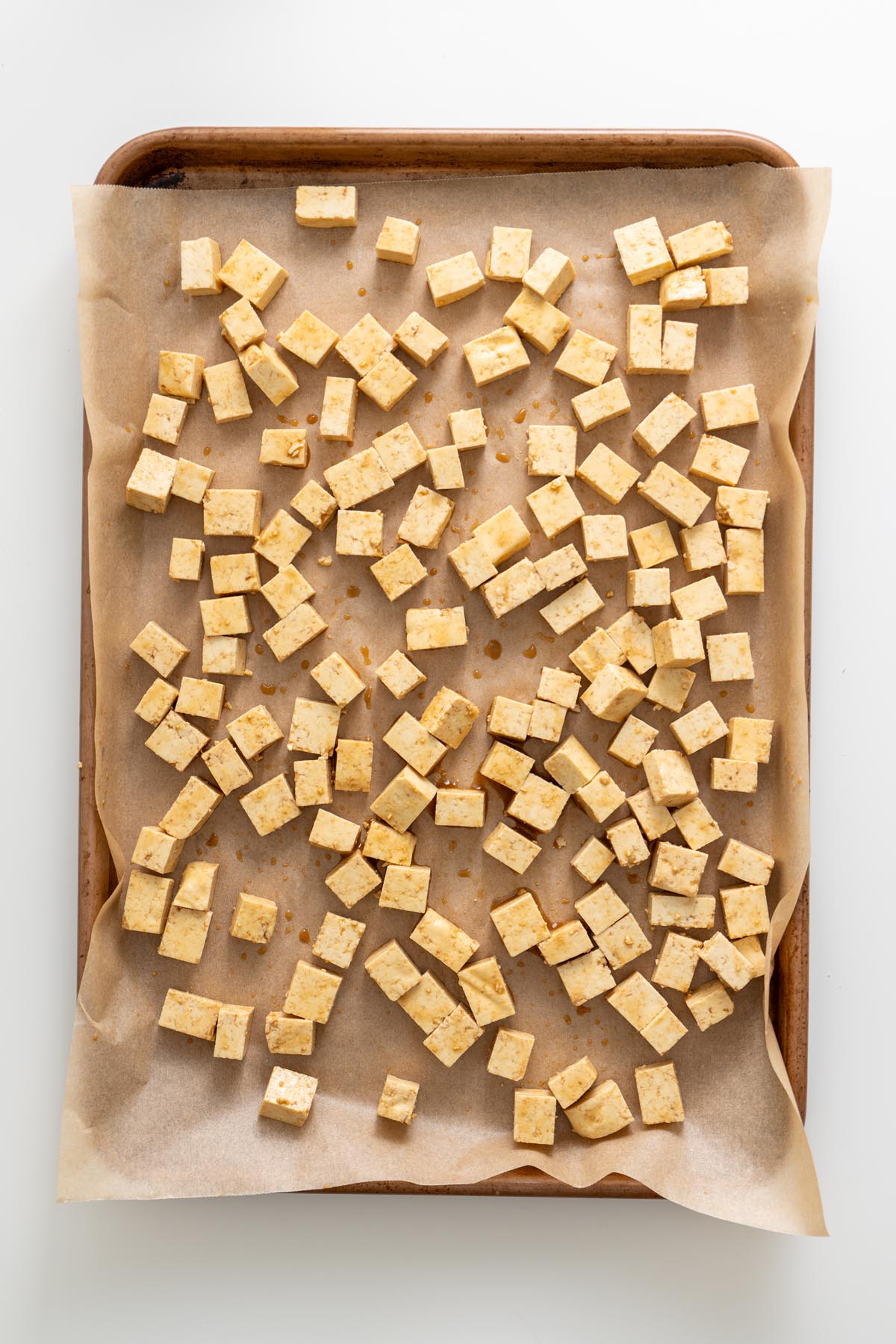 Marinated tofu cubes spread on a parchment-lined tray before baking