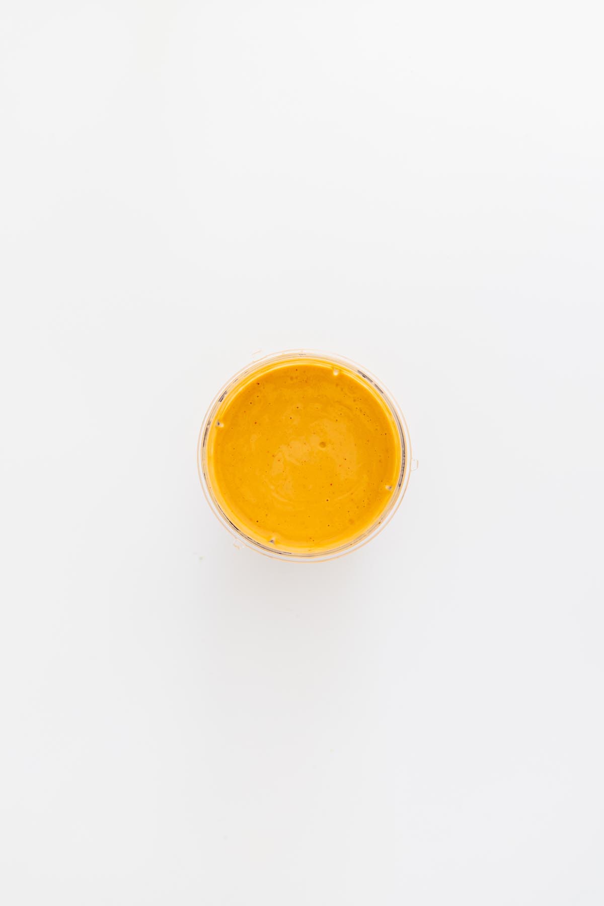 Blended creamy peanut lime sauce in a clear cup on a white background