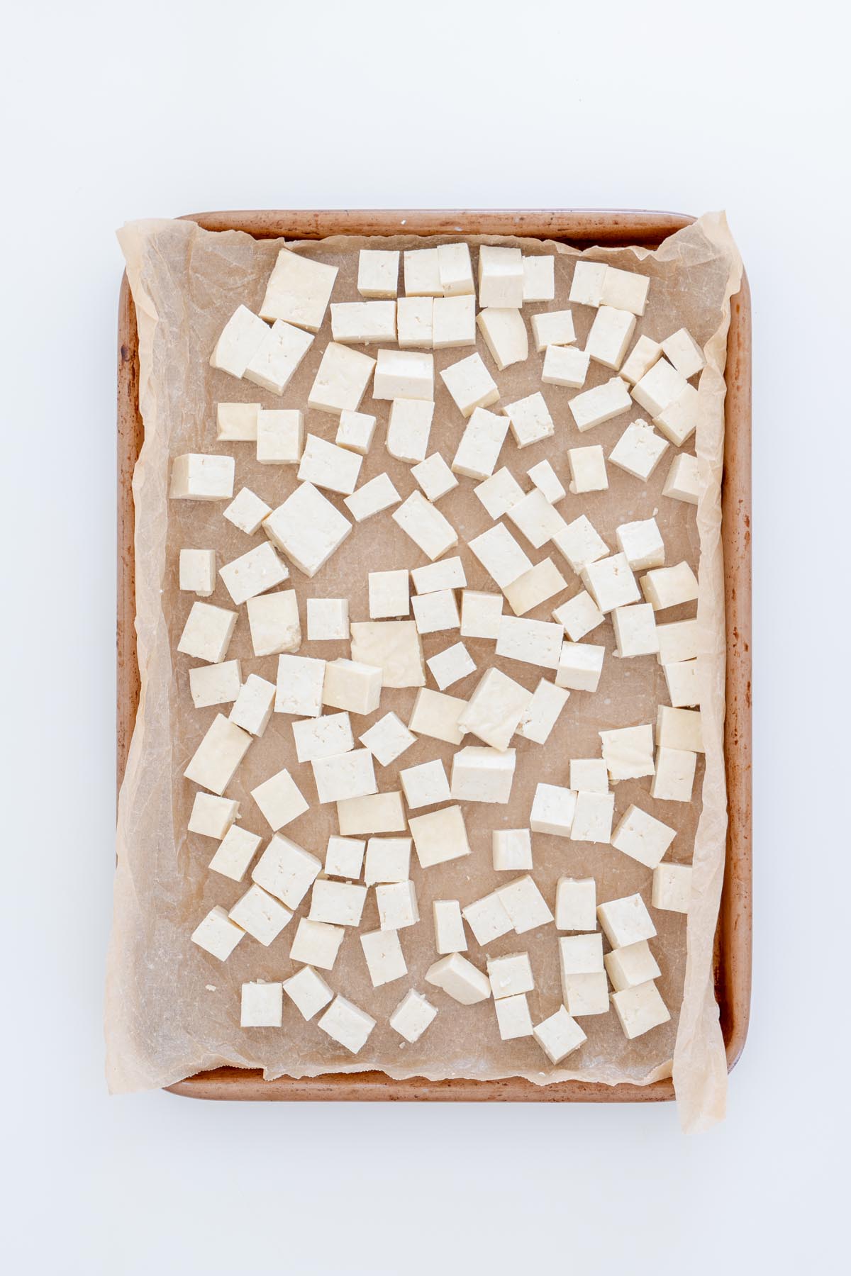 Uncooked tofu cubes spread out on a parchment-lined baking tray
