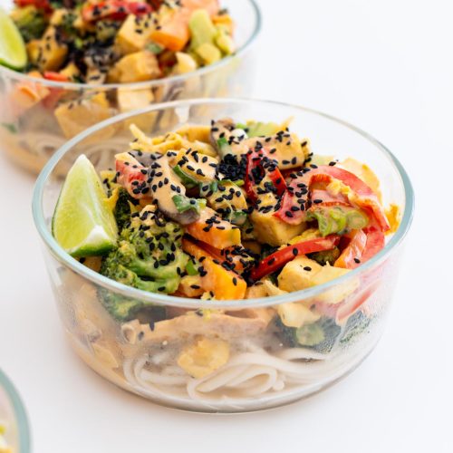 eal prep containers filled with veggie noodle stir fry topped with black sesame seeds and lime wedges
