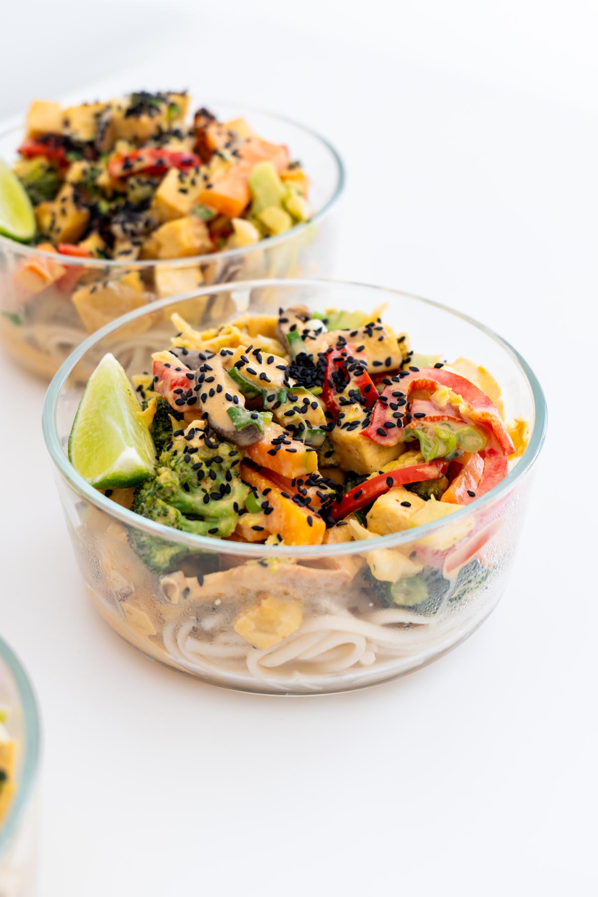 eal prep containers filled with veggie noodle stir fry topped with black sesame seeds and lime wedges