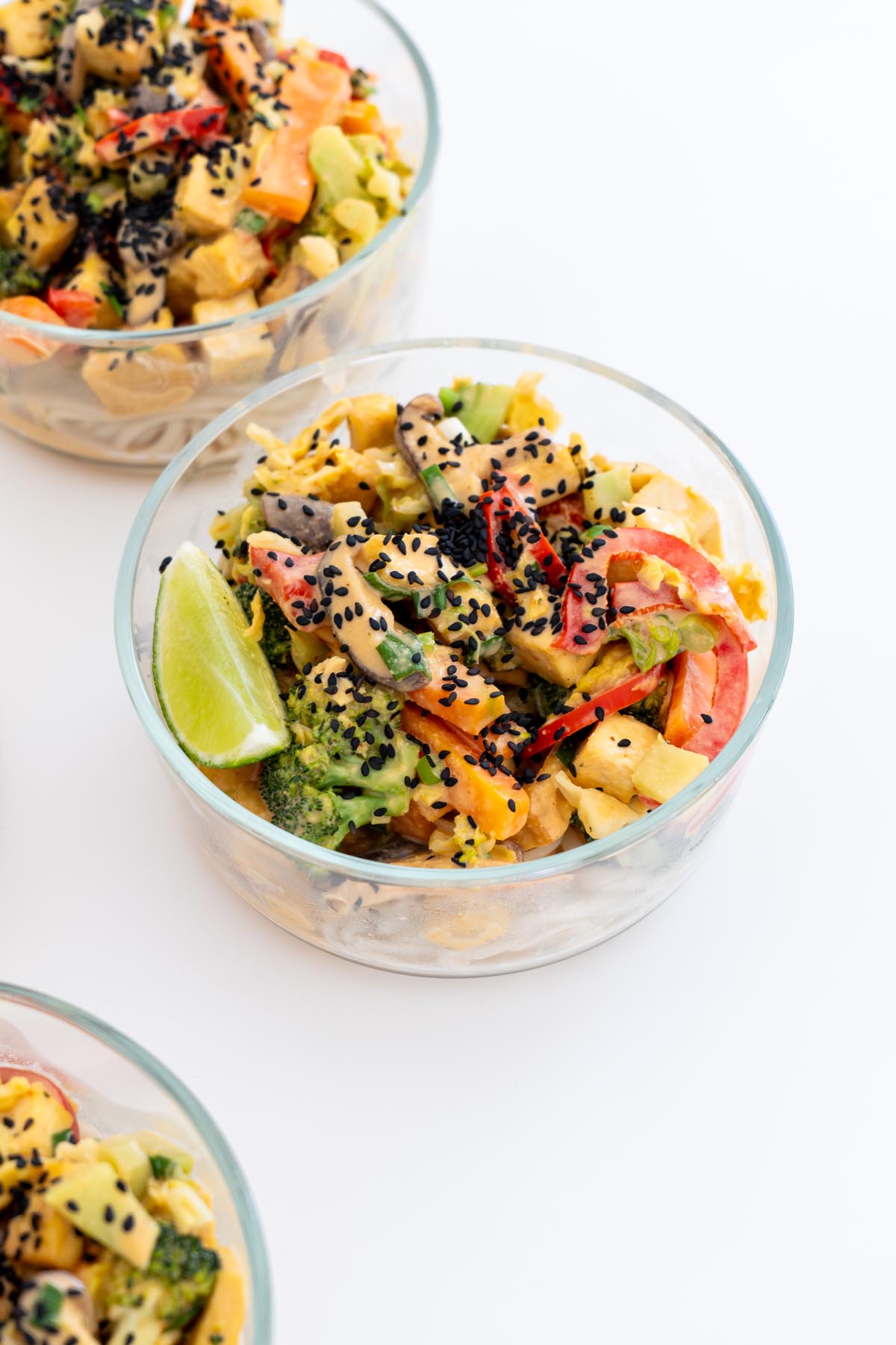Close-up of veggie noodle stir fry in a glass meal prep container with tofu, vegetables, and black sesame seeds