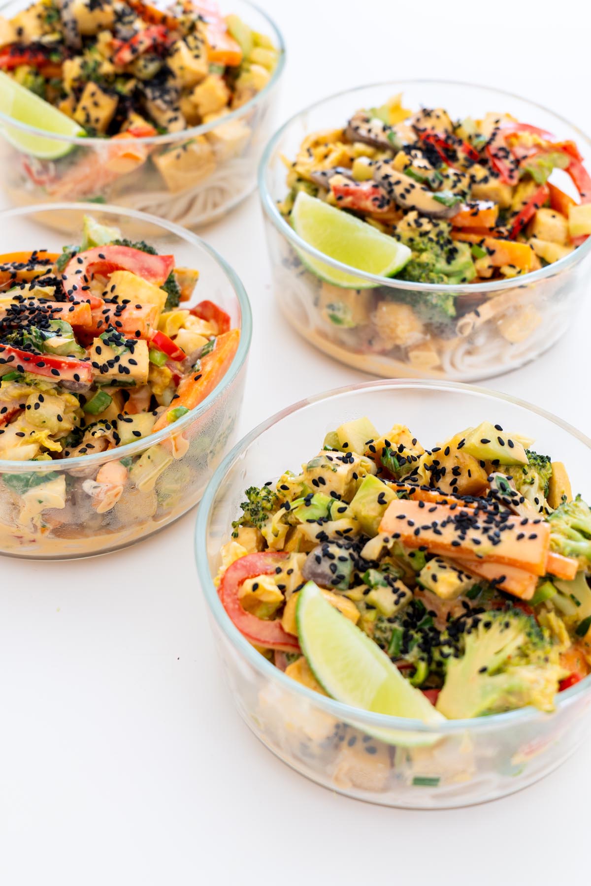 Multiple glass meal prep containers filled with veggie noodle stir fry with tofu, vegetables, and sesame seeds