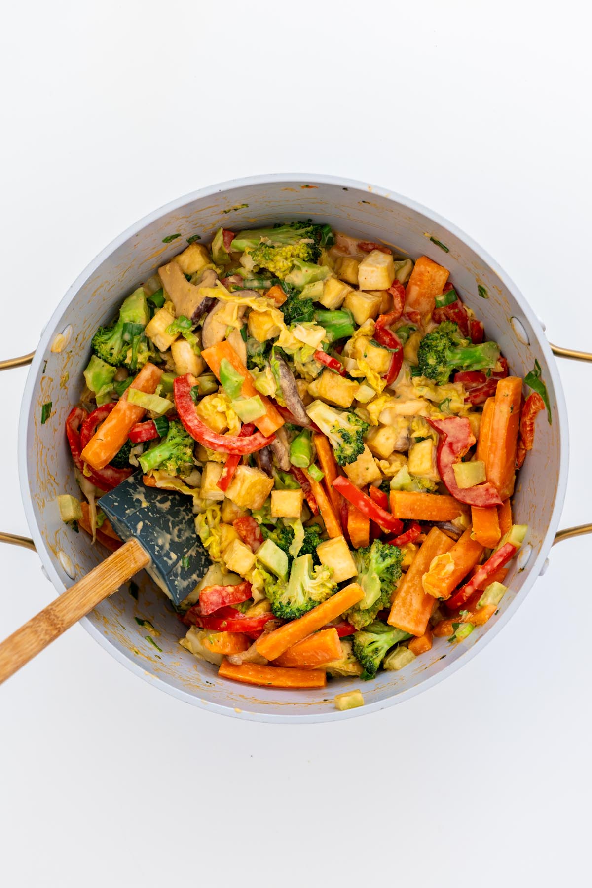 Large pot filled with stir-fried tofu, broccoli, carrots, mushrooms, cabbage, and red bell pepper coated in peanut lime sauce