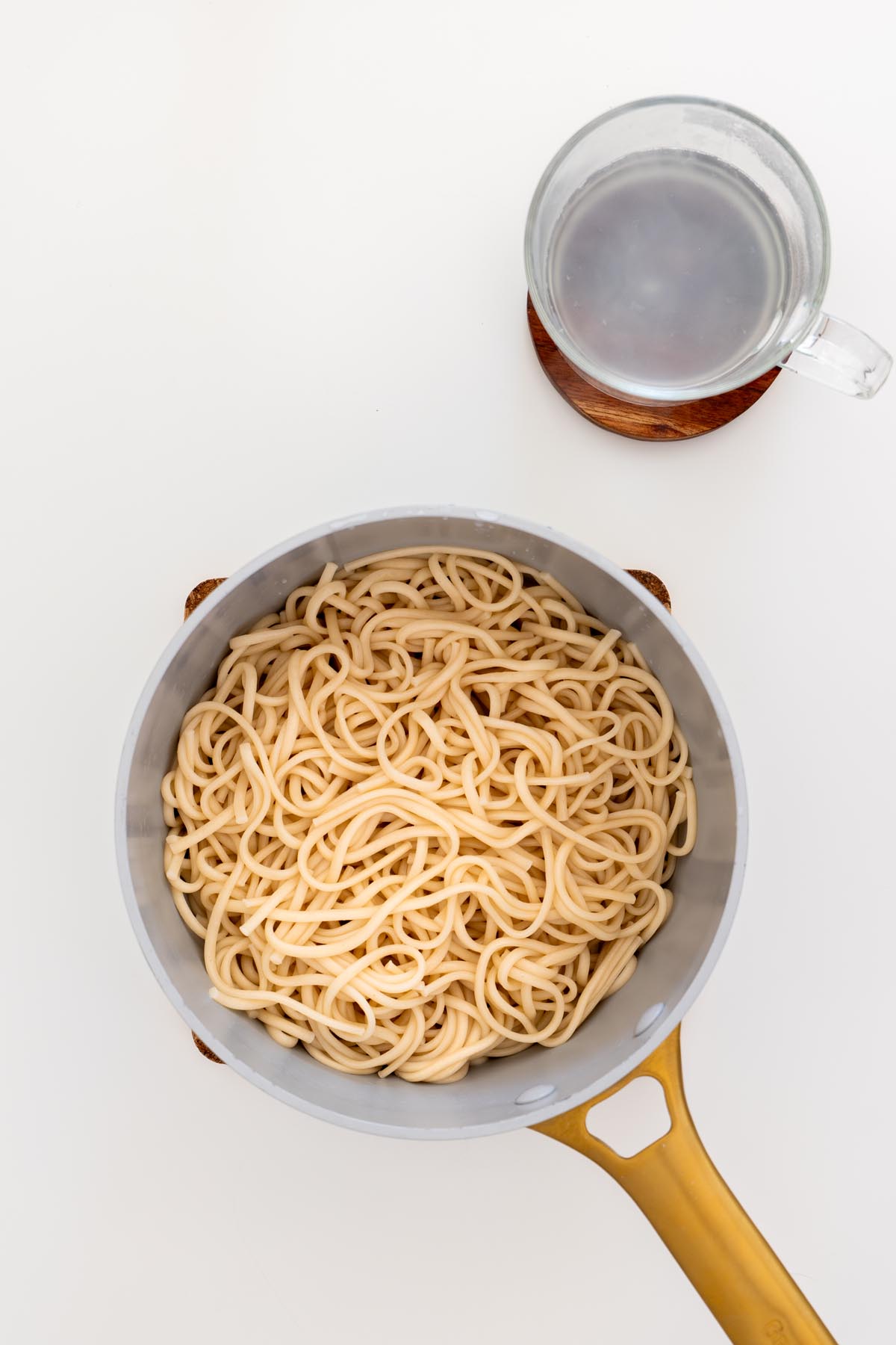 Cooked udon noodles in a pot with reserved cooking water in a glass cup beside it