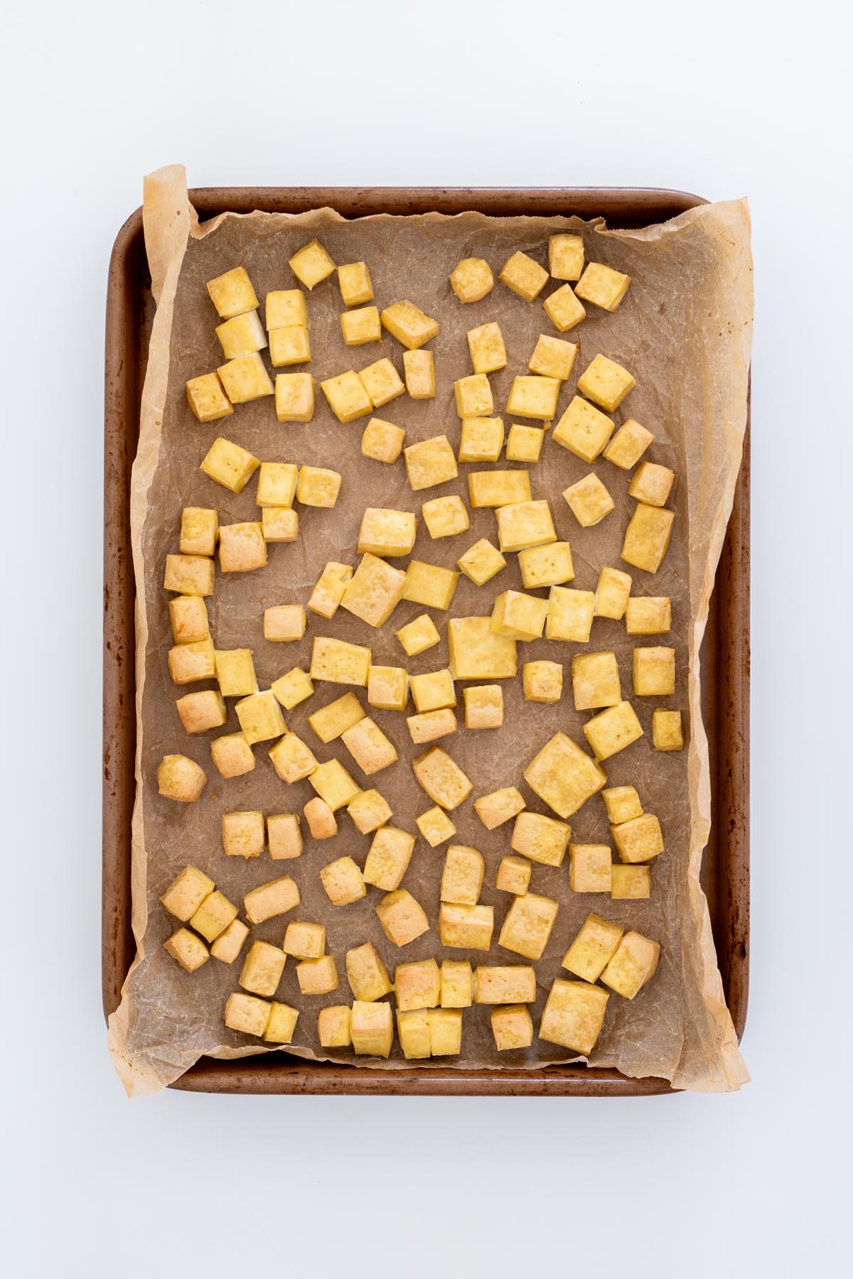 Baked golden tofu cubes on a parchment-lined baking tray