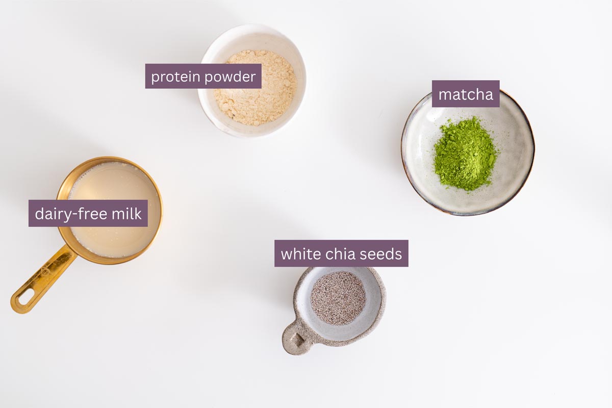 Vibrant ingredients for a blended matcha chia pudding including dairy-free milk, protein powder, matcha, and white chia seeds on a white surface.