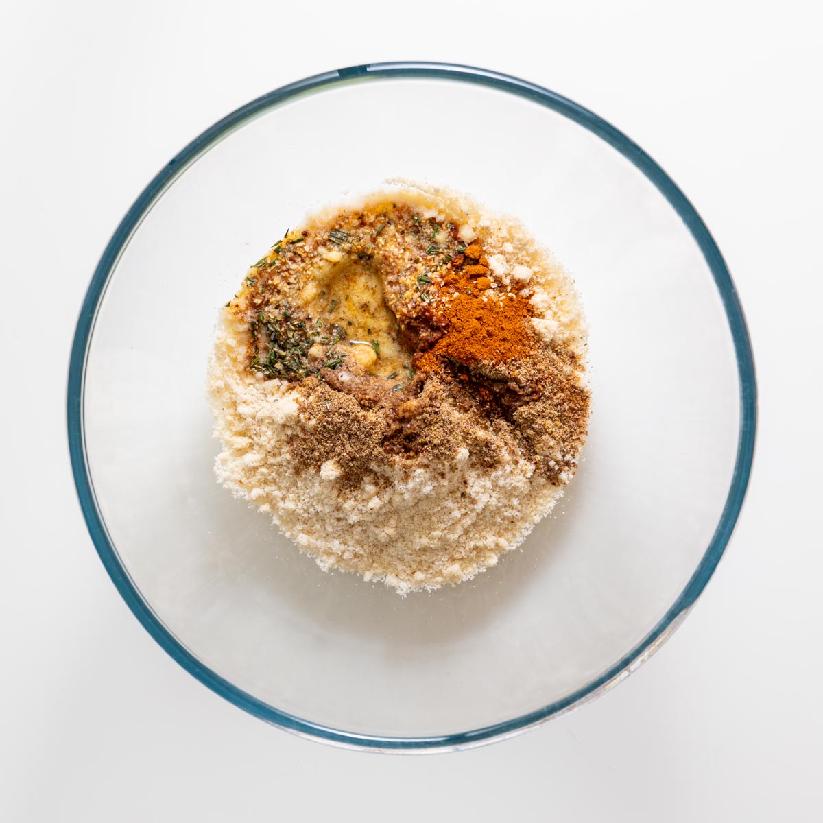 Almond flour, ground flaxseed, rosemary, garlic granules, sweet paprika, sea salt, olive oil, and water in a glass bowl before mixing.