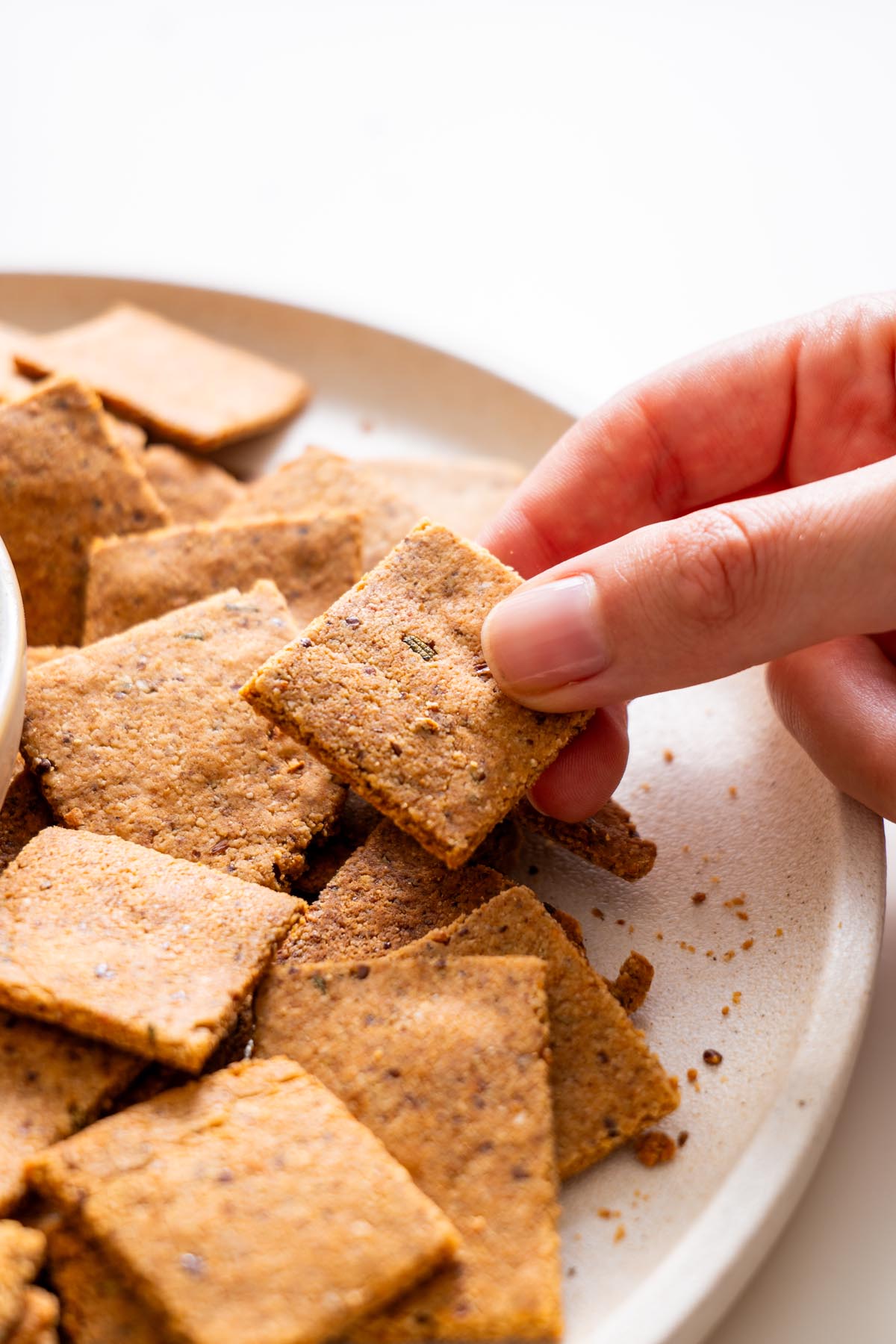 Sarah Cobacho holding a square almond flour rosemary cracker above a plate of baked crackers.