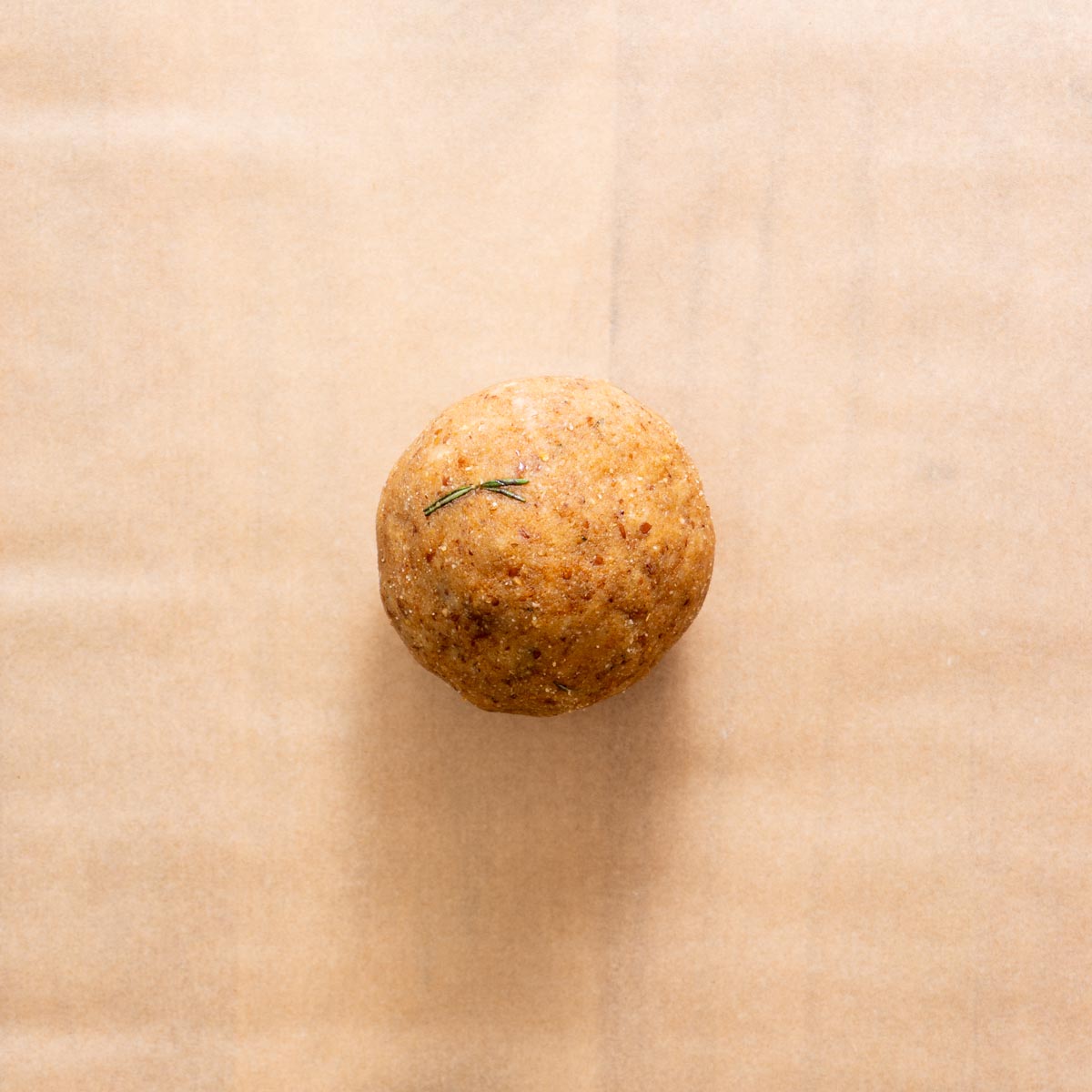 Almond flour rosemary cracker dough ball on parchment paper, ready to roll.