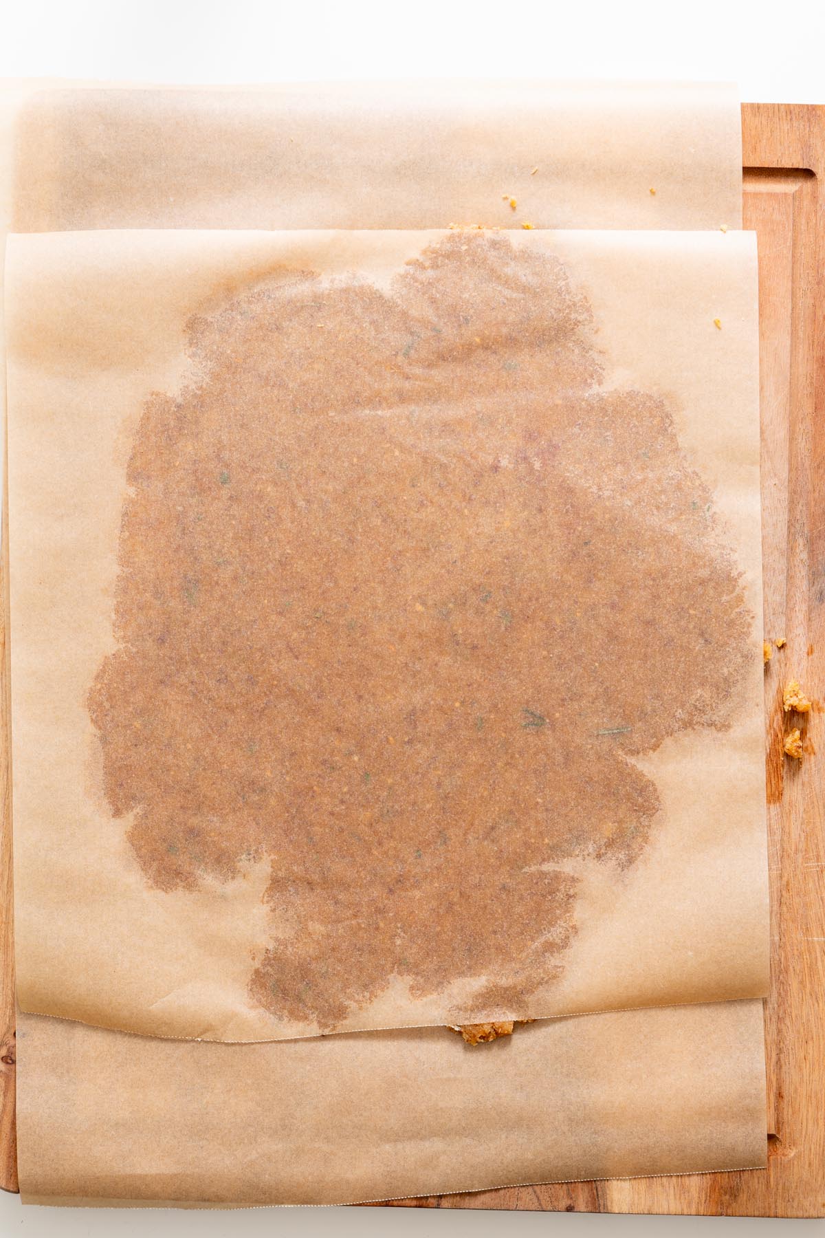 Almond flour rosemary cracker dough rolled thin between two sheets of parchment paper on a wooden board.