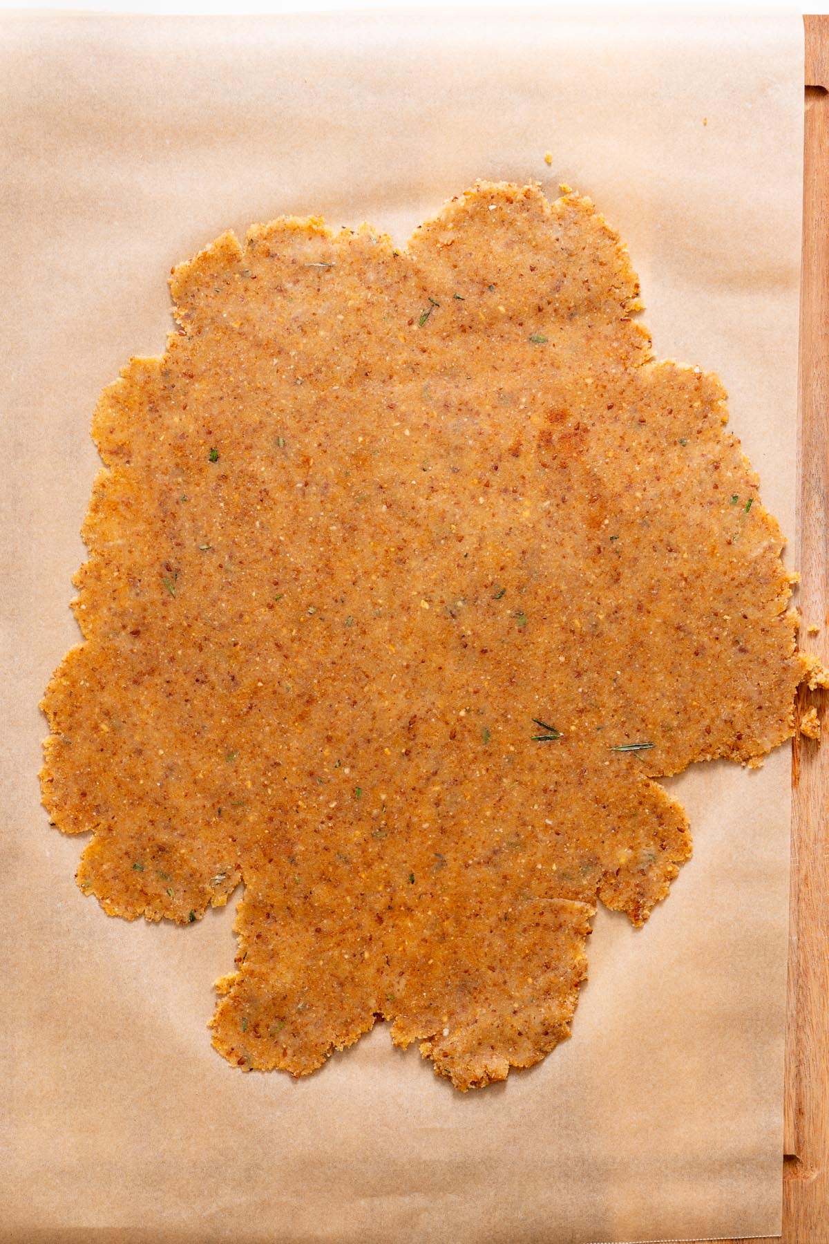 Rolled almond flour rosemary cracker dough on parchment paper, evenly flattened and ready to score.